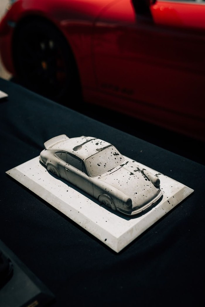 A 3D-printed car model on a plinth beside a red car.